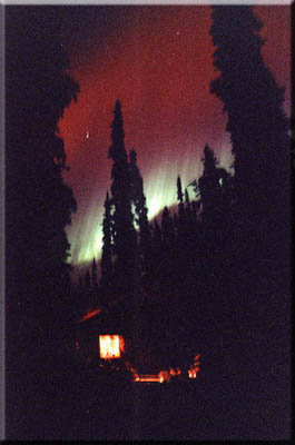 Red and green northern lights above a log cabin.